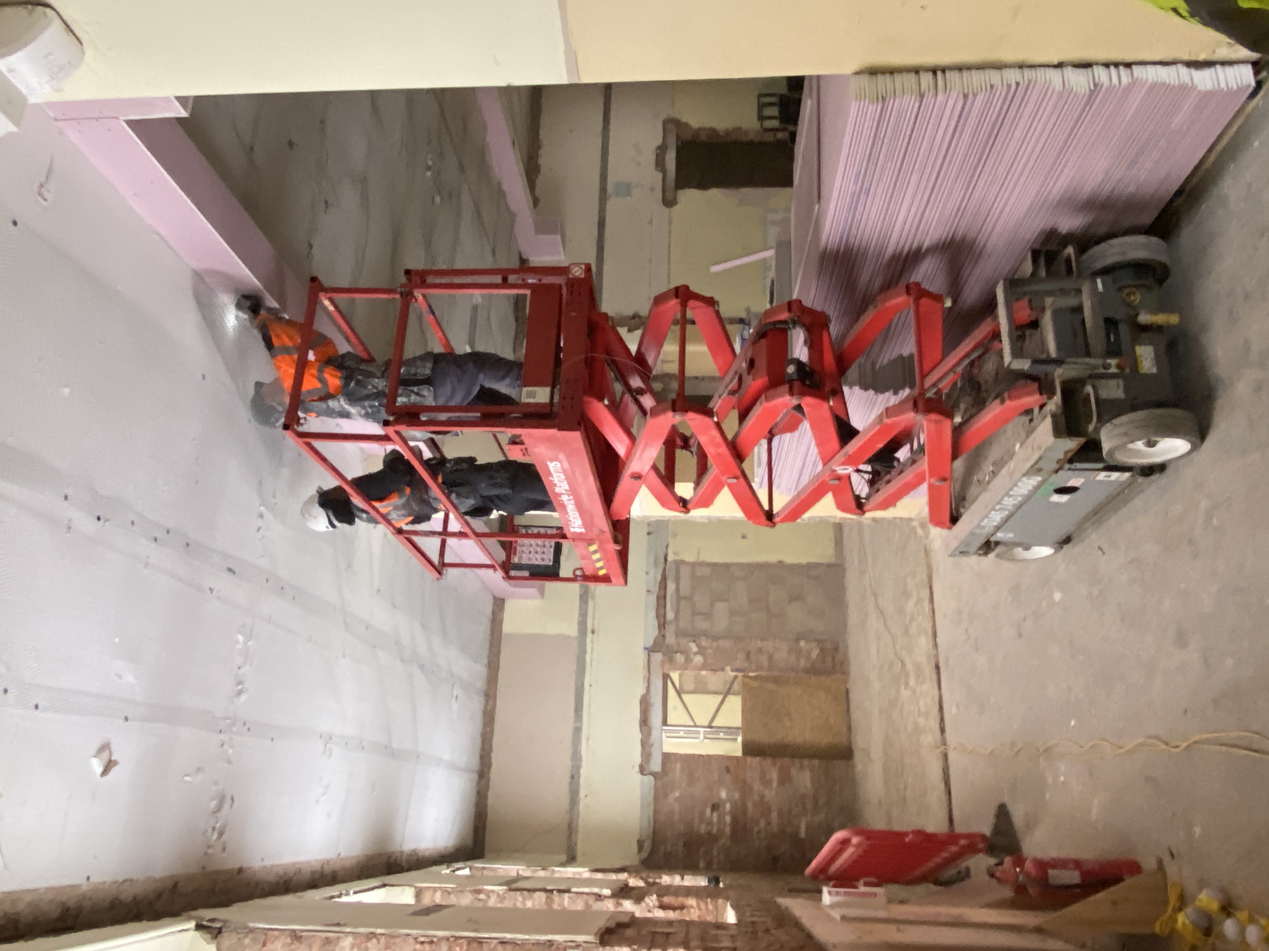 Photo of the inside of Gateway Lodge. Workers are on a telescopic platform working to apply mesh to the ceiling prior to replastering.