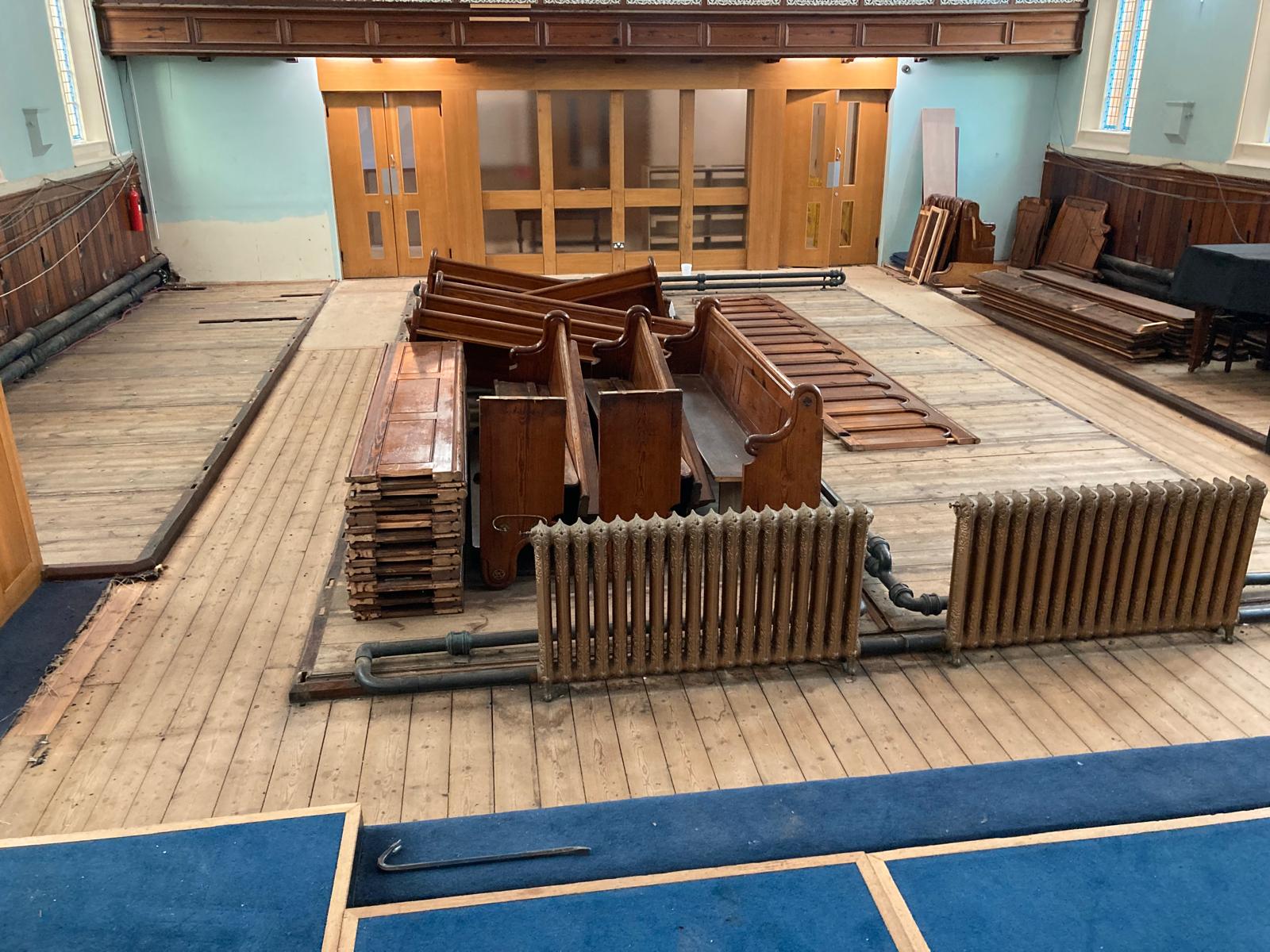 The interior of Ashbourne Methodist Church with bare wooden floors and pews carefully dismantled and stacked in the middle of the floor. The pews will be re-purposed for use within the new building.